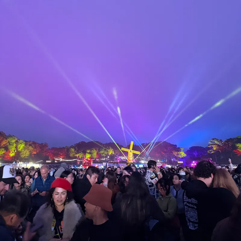 A crowd at an outdoor music festival under purple light beams