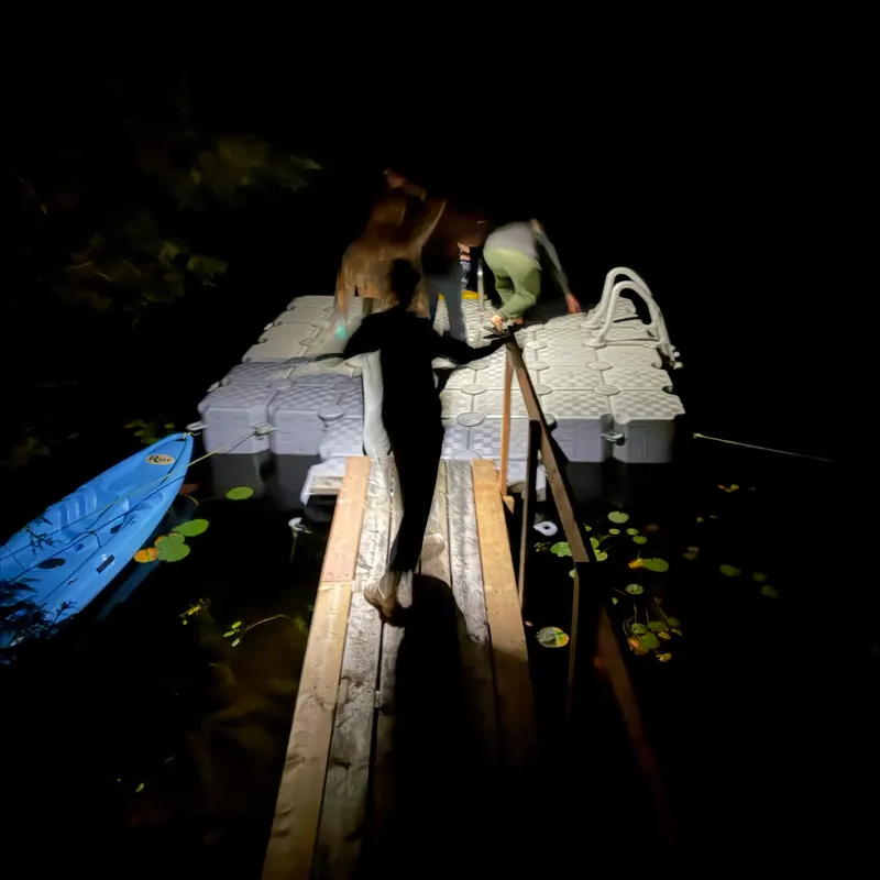 Friends on a floating dock at night beside a blue kayak