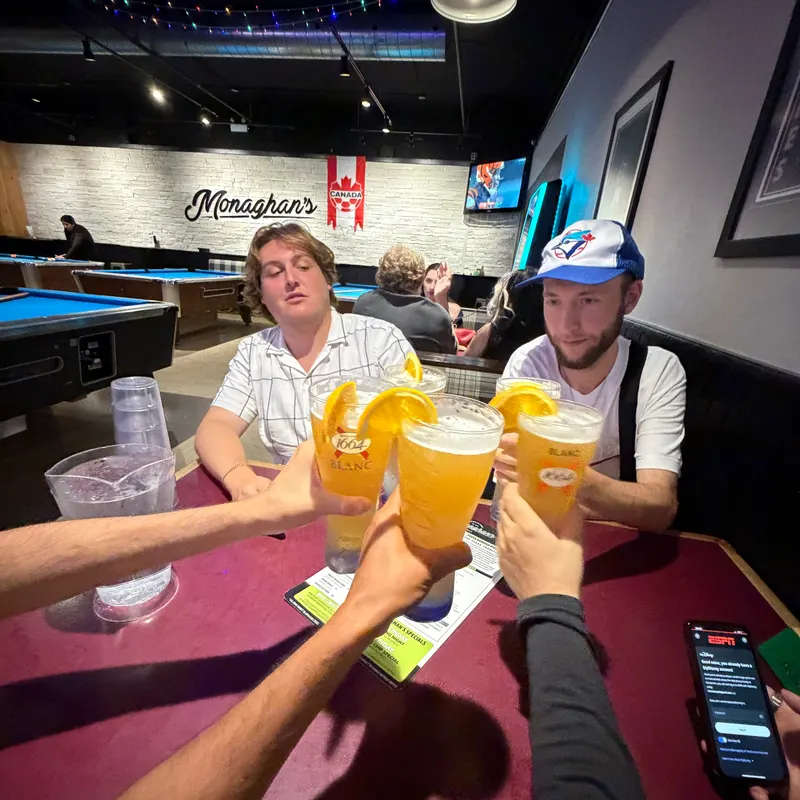 Friends clinking glasses of beer with orange slices at a pool hall