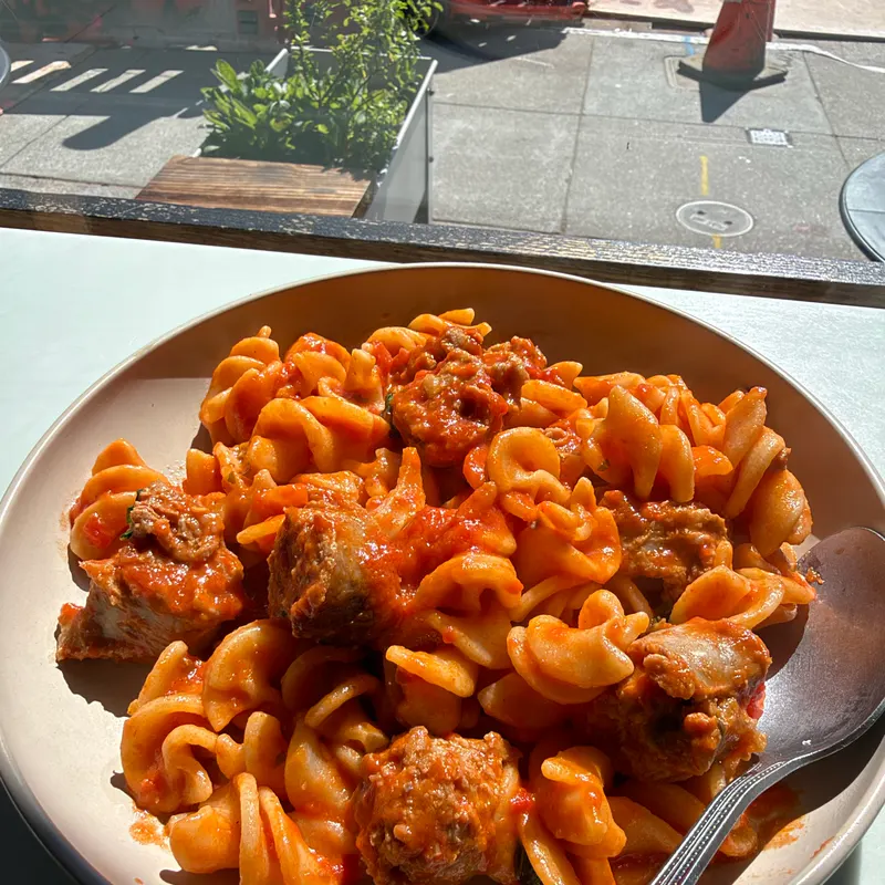 A bowl of fusilli and meatballs in tomato sauce by a sunny window