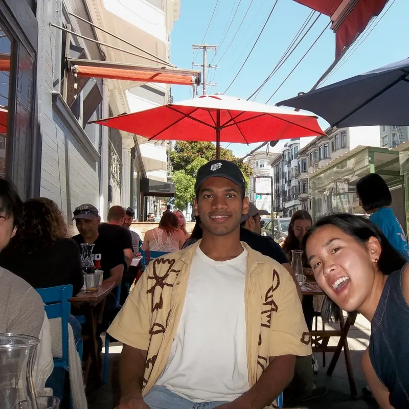 Two friends smiling at a sidewalk café table under red umbrellas